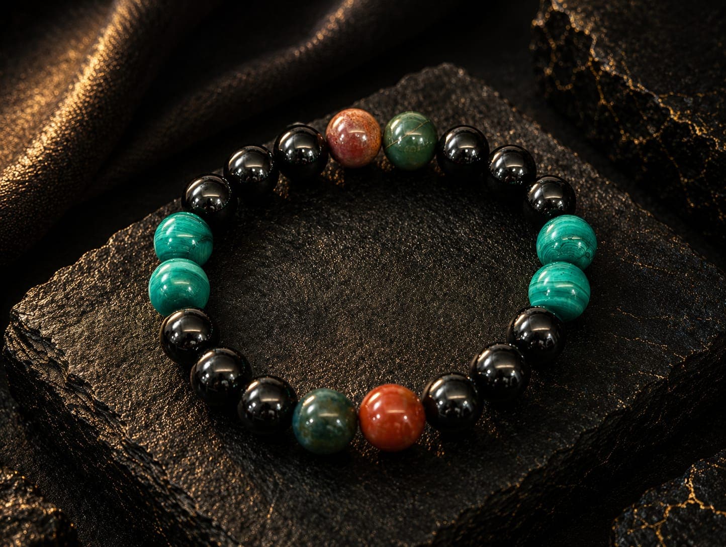 Polished black, green, and red stone bead bracelet resting on dark textured stone.