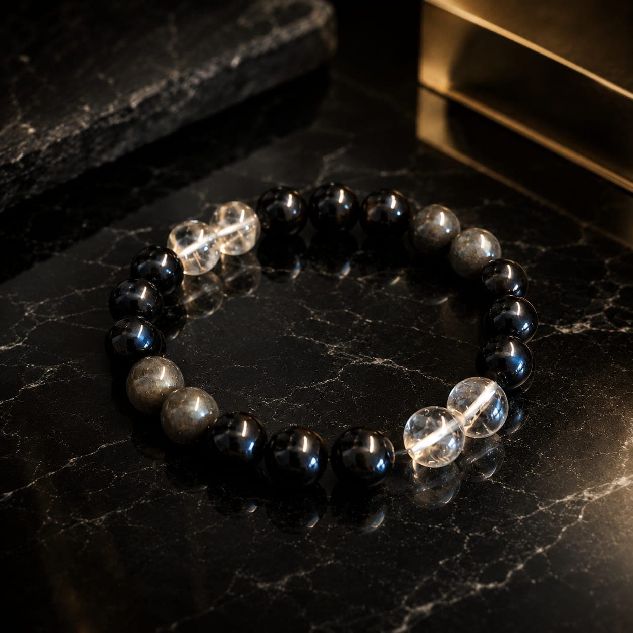Beaded bracelet featuring black, clear quartz, and labradorite stones on a dark marble surface.