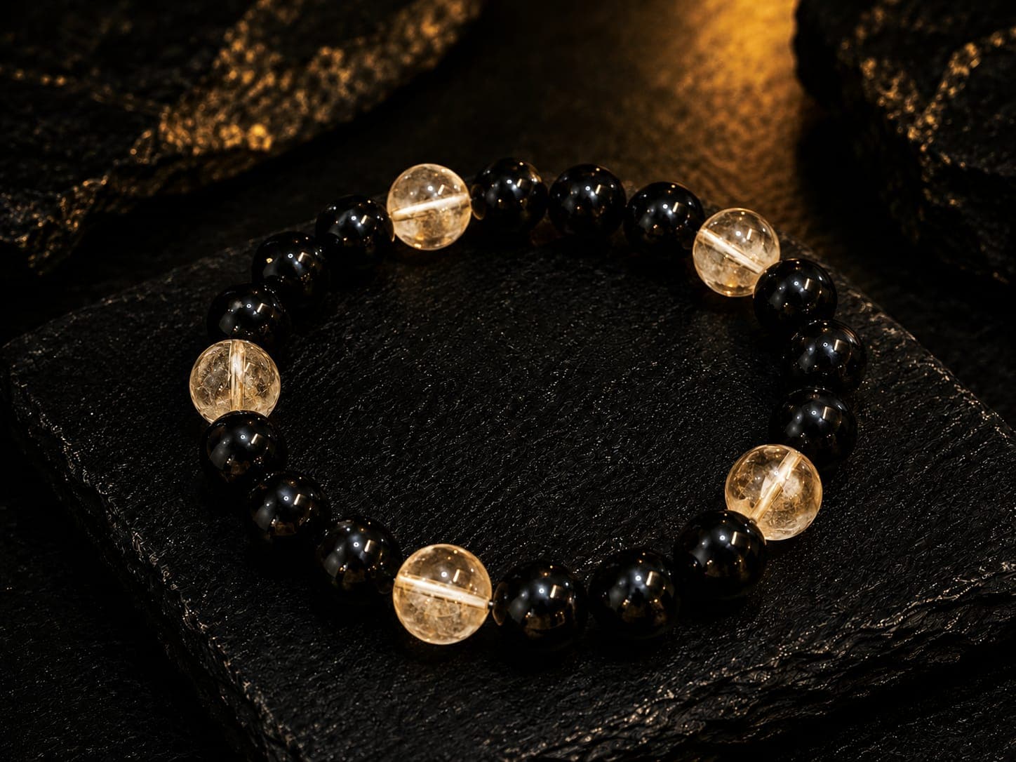 Polished black and translucent yellow beads form a bracelet on a dark, textured stone surface.