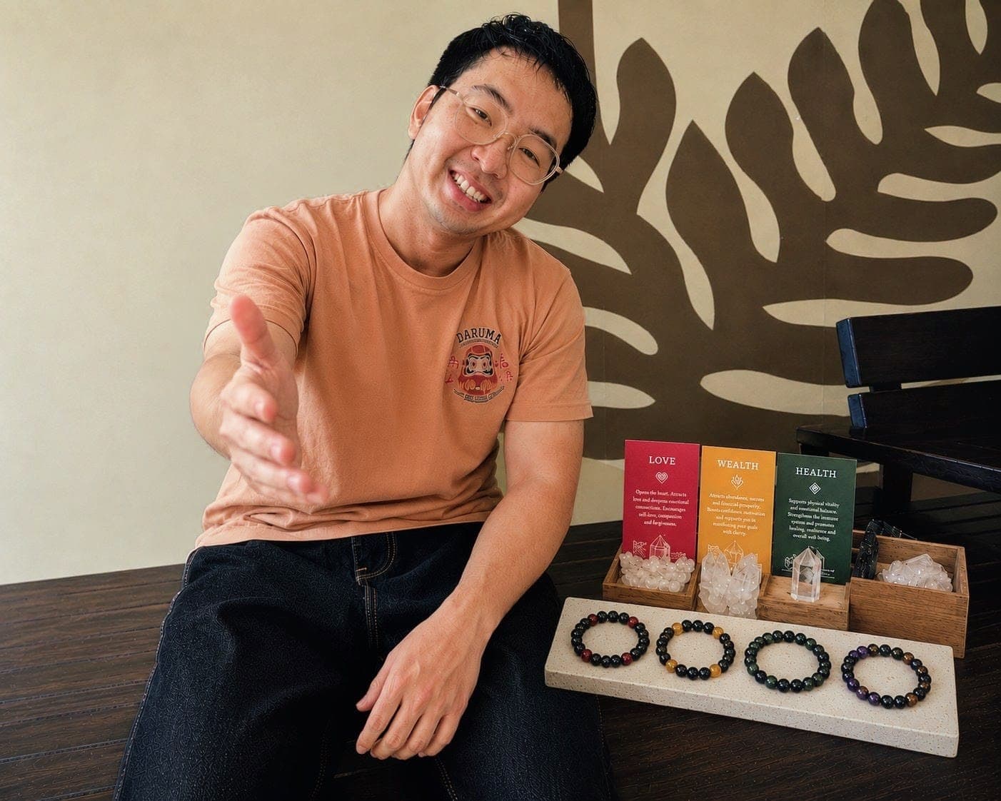 Smiling man reaches out his hand beside a display of beaded bracelets and crystals.