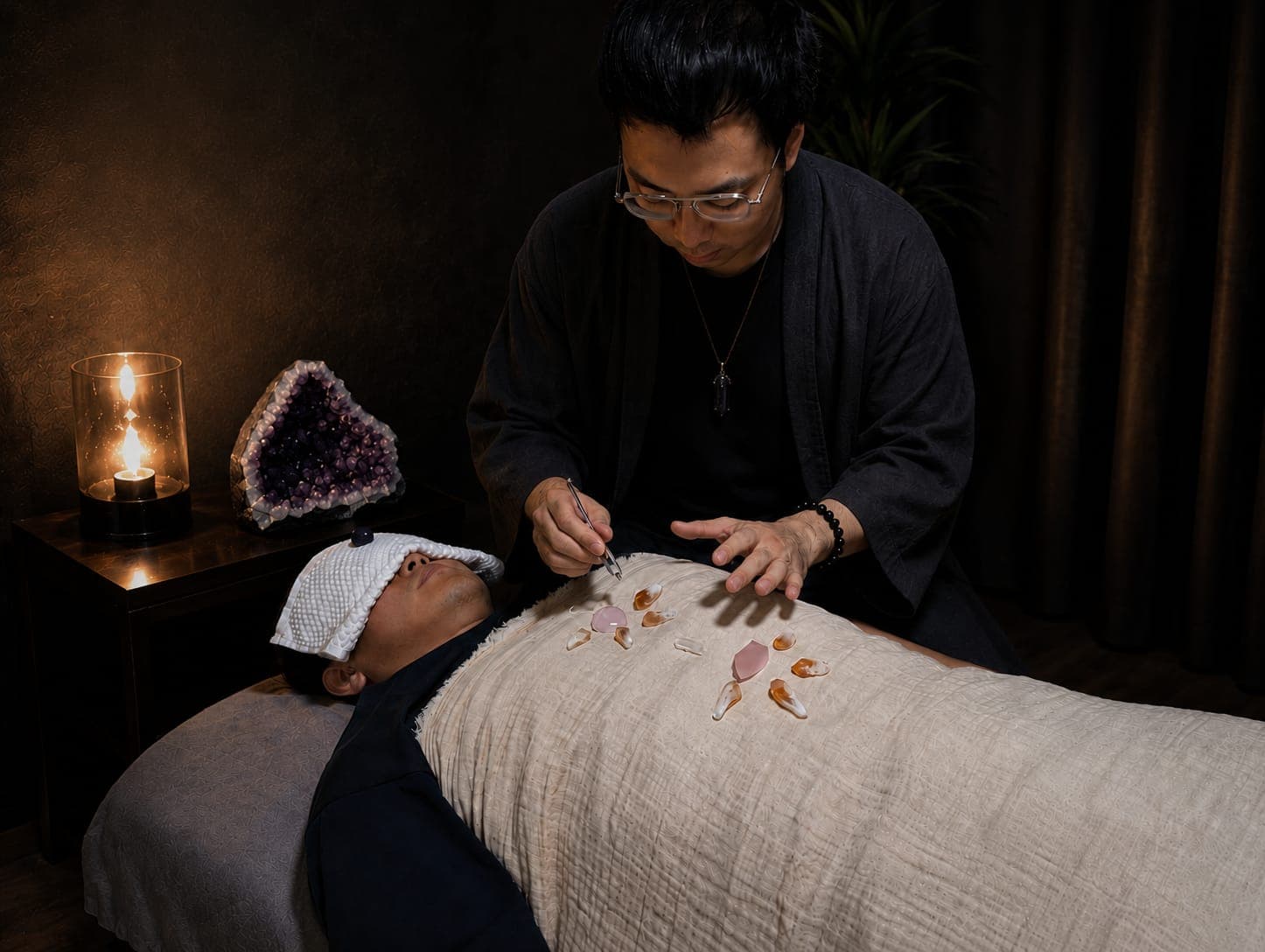 Practitioner placing healing crystals on a person's chest in a dimly lit, candlelit room.