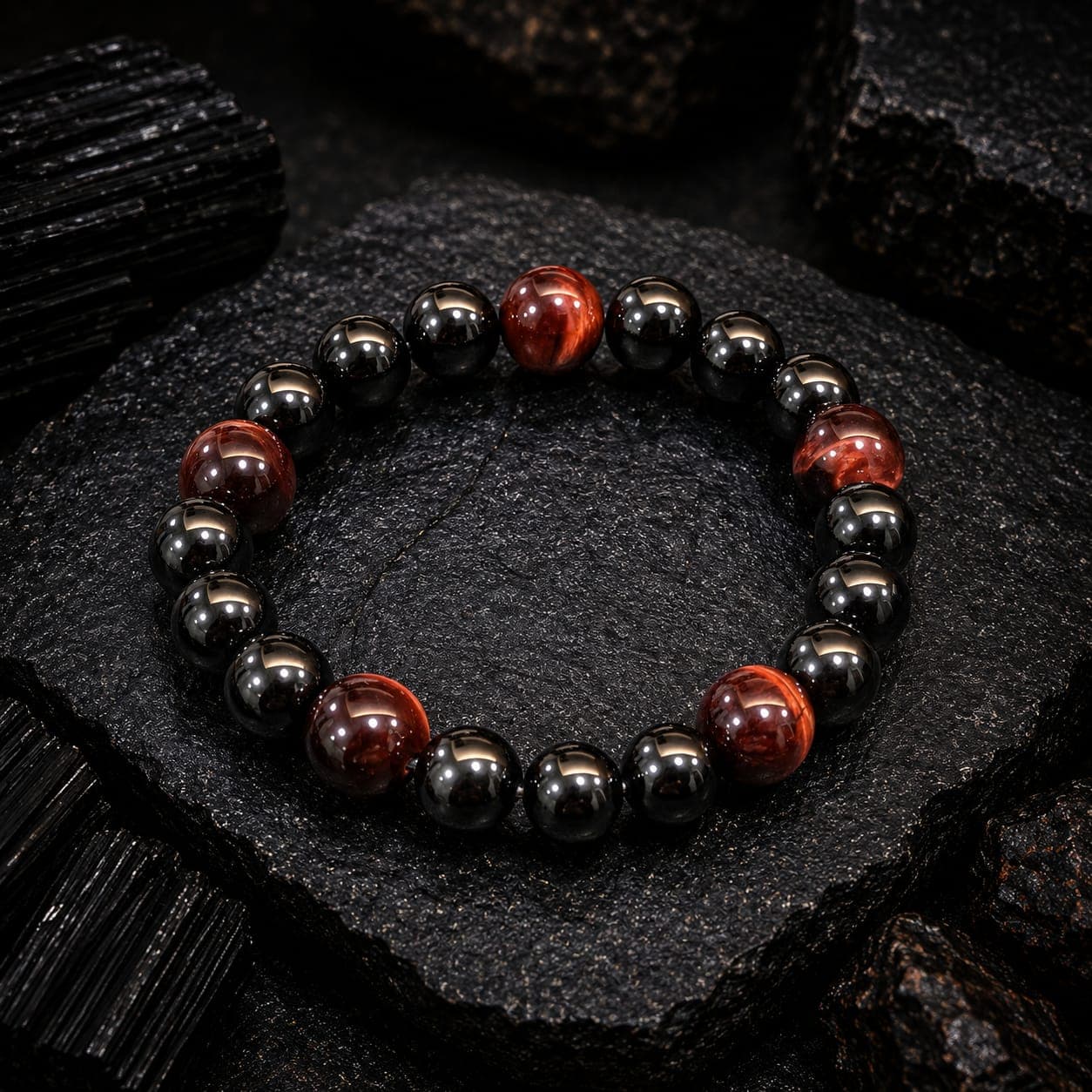 Polished black and red tiger's eye beaded bracelet resting on a dark, textured mineral surface.