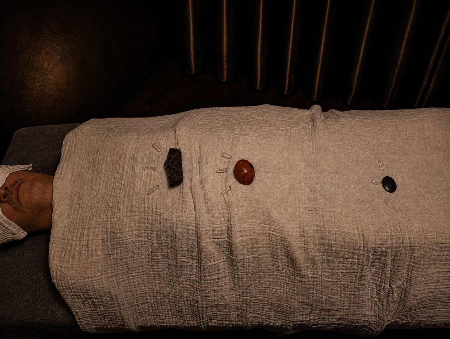 Healing crystals and stones arranged on a person lying under a light-colored textured cloth.