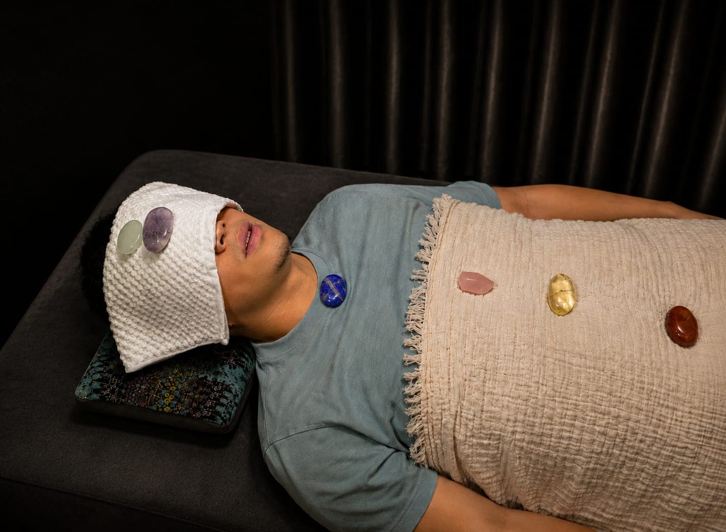 Man lying down with colorful healing crystals placed on his forehead, throat, and chest.